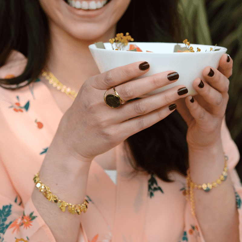 Une jeune femme souriante avec des bijoux bougie bijou sur les poignets, autour du cou et aux doigts. Elle tient une bougie bijou orange romarin dans ses mains